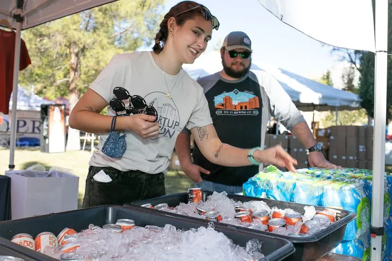 Two volunteers icing down bottles and cans in bins at an aid station table.