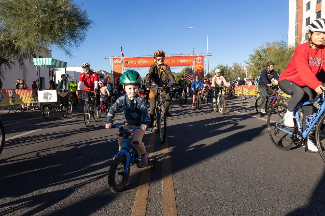 A young child on a small blue bike leading families down a closed street.