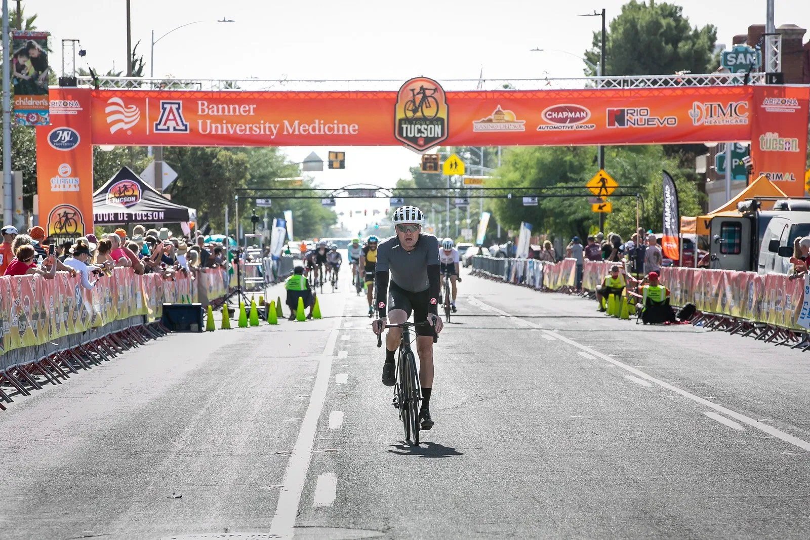 A rider coming up the finish chute, the arch behind and spectators lining the barriers on both sides.