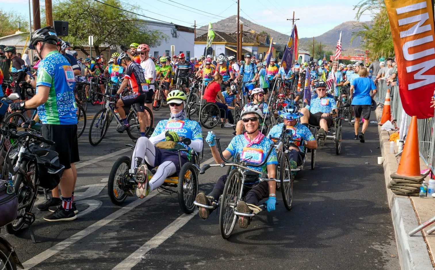 Handcyclists in the front row of a fun ride start with hundreds of riders behind them and a mountain on the skyline.