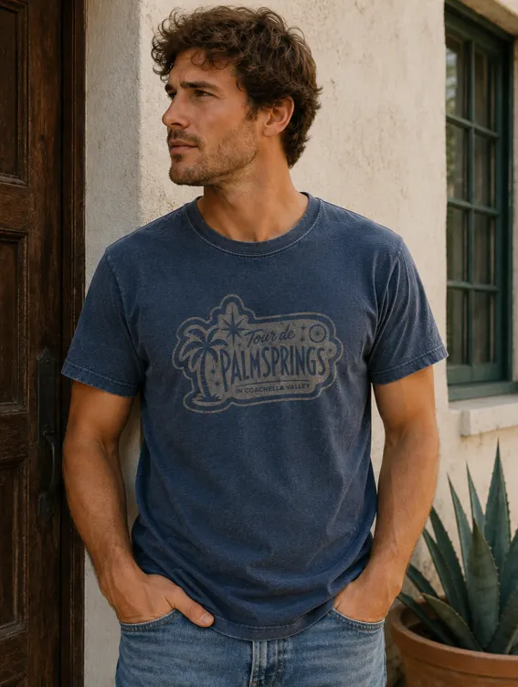 Man wearing a navy short-sleeve Tour de Palm Springs tee, leaning in a doorway
